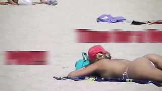 Женщина загорает в стрингах оголив сиськи на обыкновенном пляже